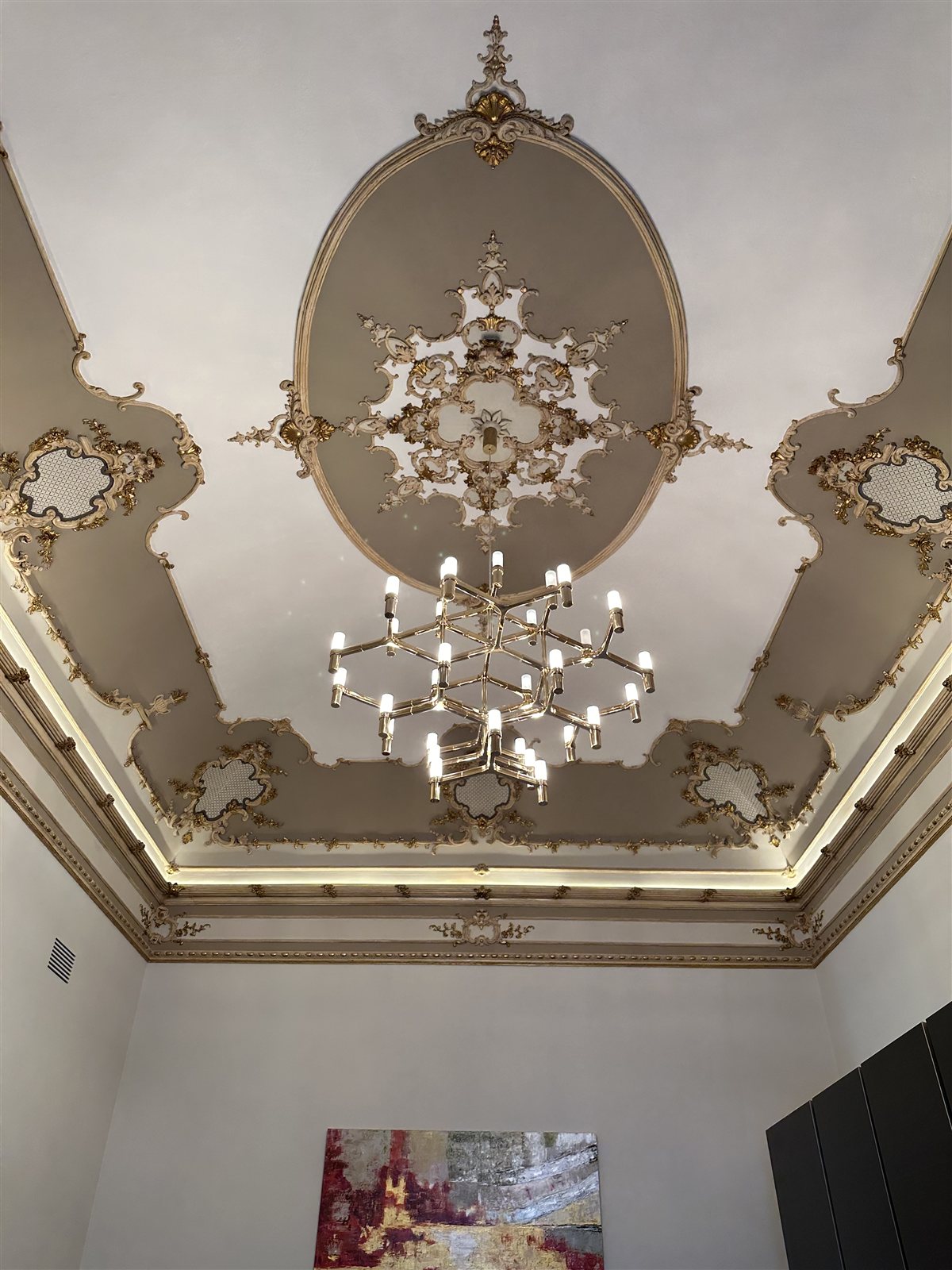 Il lampadario decorativo sotto il rosone di stucco: un elemento scenico, non la fonte principale di luce.